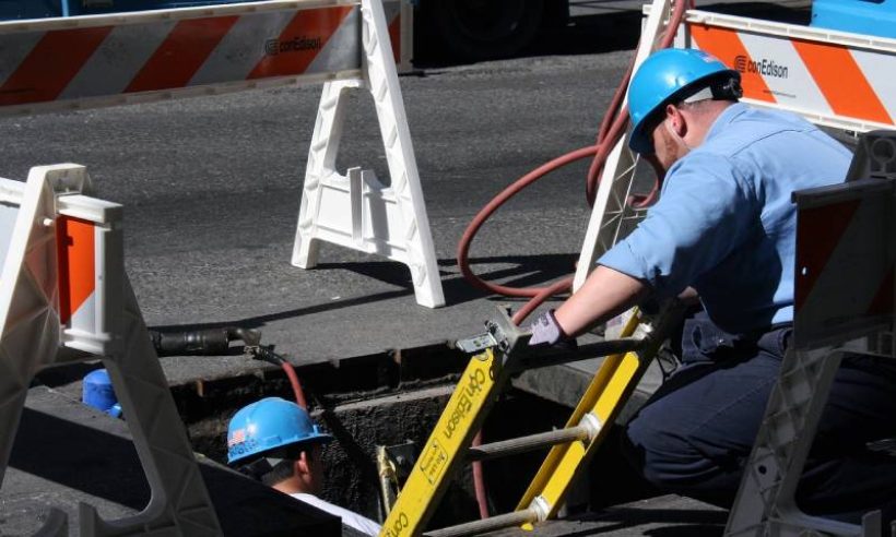 Construction workers wearing hard hats and working on a manhole.