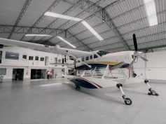 A large white amphibious seaplane (Cessna Caravan-type aircraft with floats) is parked inside a spacious modern hangar. (Photo: Alma Air)