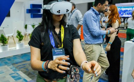 Andicom 2025 attendee wearing a VR headset at the tech exhibition, with the conference booth and other attendees visible in the background.