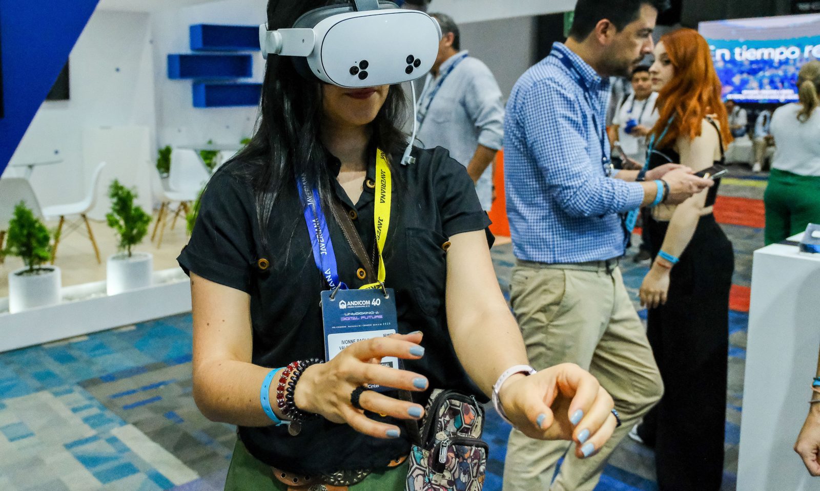 Andicom 2025 attendee wearing a VR headset at the tech exhibition, with the conference booth and other attendees visible in the background.