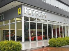 A modern glass Ferrari showroom with the iconic Ferrari logo and red sports cars visible inside, along with the landscaped entrance in Bogotá. (Photo: EEIM via Wikimedia Commons)