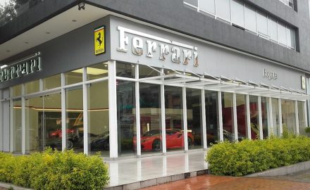 A modern glass Ferrari showroom with the iconic Ferrari logo and red sports cars visible inside, along with the landscaped entrance in Bogotá. (Photo: EEIM via Wikimedia Commons)