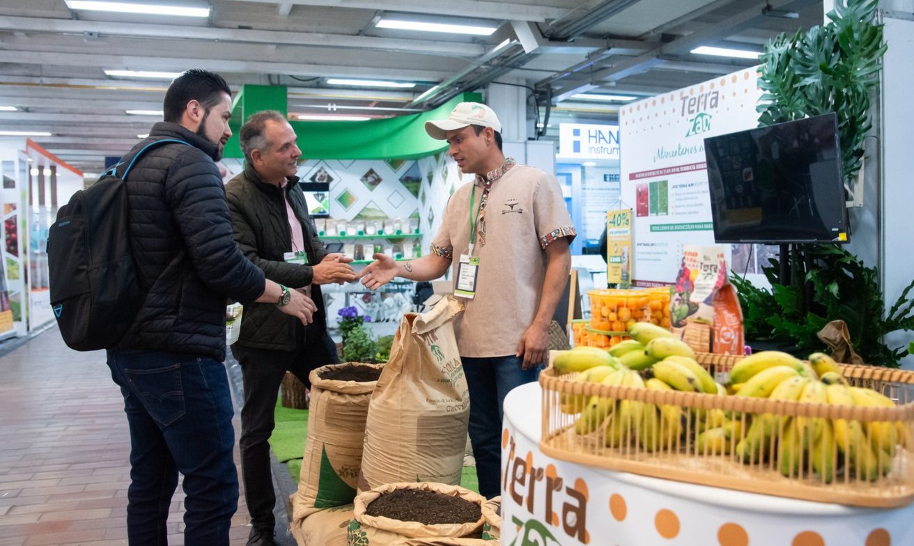 Exhibitors and visitors networking at a Terra Zan booth during Expo Agrofuturo, featuring agricultural products including bananas, soil amendments, and fertilizer displays. (Photo : Expo Agrofuturo)