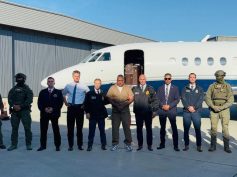 Geovany Andrés Rojas, alias Araña, stands among US law enforcement officials in front of a jet