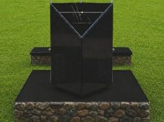 Black marble memorial monolith on a stone base in a grass field