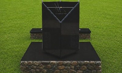 Black marble memorial monolith on a stone base in a grass field