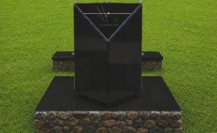 Black marble memorial monolith on a stone base in a grass field