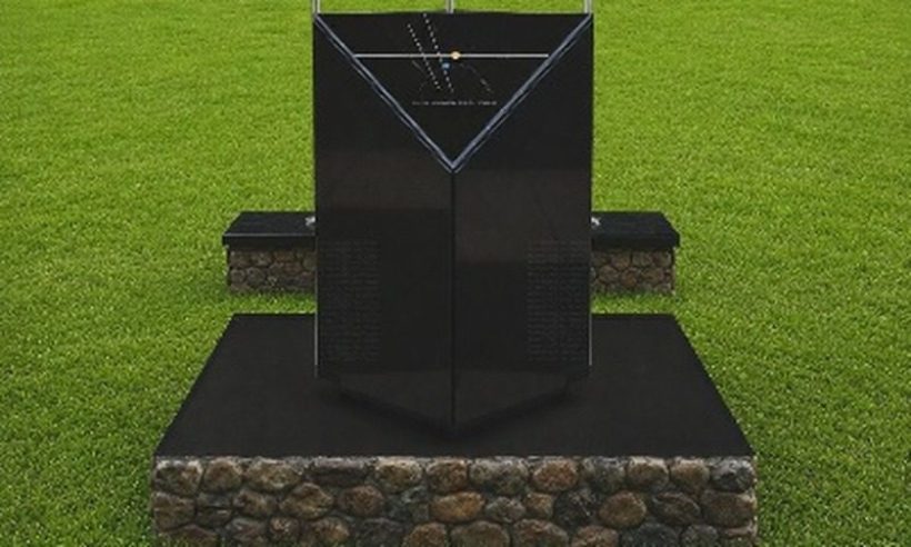 Black marble memorial monolith on a stone base in a grass field