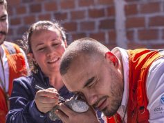 A man in a Collective Mining vest examines a rock sample with a hand lens while two others look on