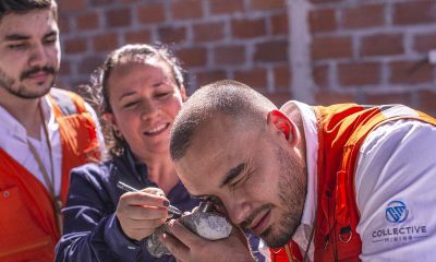 A man in a Collective Mining vest examines a rock sample with a hand lens while two others look on