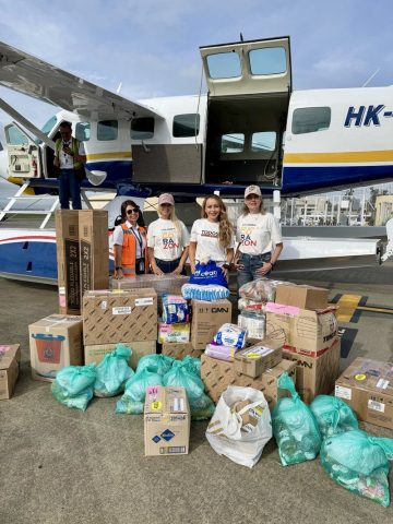 Mónica Gil Ryan and three others stand with donated diapers, food and supplies in front of a floatplane