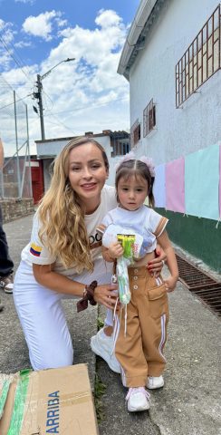 Mónica Gil Ryan kneels beside a young girl holding a donated kit with a toothbrush and snacks