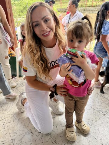 Mónica Gil Ryan kneels beside a toddler holding a hygiene kit with toothpaste