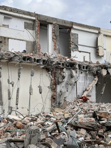 Close view of a collapsed multistory building with exposed brick, broken slabs and dangling cables over rubble