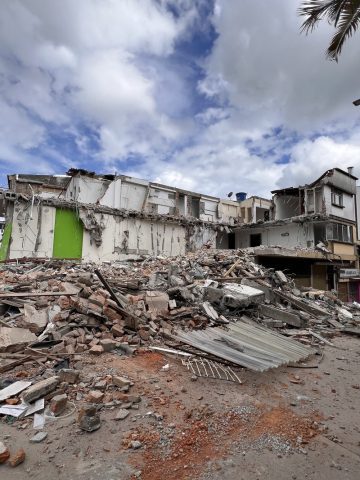 Rubble from several collapsed buildings spills across a street under a partly cloudy sky