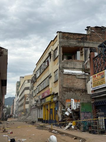 Excavator demolishes a quake-damaged building on a cordoned-off commercial street lined with cracked facades