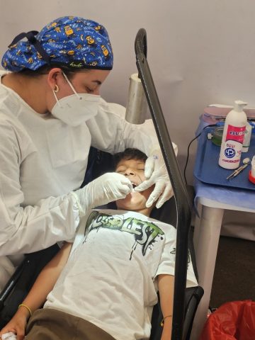 Dentist in mask and gown examines a boy’s teeth in a temporary clinic