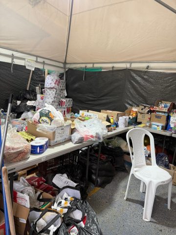 Tent filled with donated toilet paper, food, pet food, toiletries and bags of clothing on folding tables