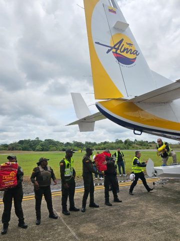 Uniformed officers pass bags of donated supplies in a line beside the tail of an Alma Air aircraft