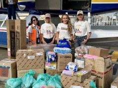 Mónica Gil Ryan and three others stand with donated boxes and bags of supplies in front of a floatplane