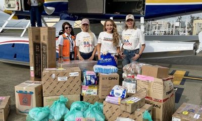 Mónica Gil Ryan and three others stand with donated boxes and bags of supplies in front of a floatplane