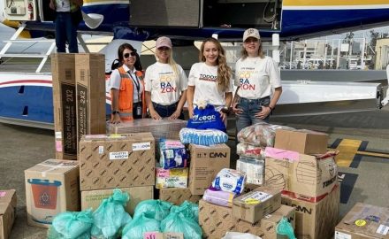 Mónica Gil Ryan and three others stand with donated boxes and bags of supplies in front of a floatplane