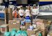 Mónica Gil Ryan and three others stand with donated boxes and bags of supplies in front of a floatplane