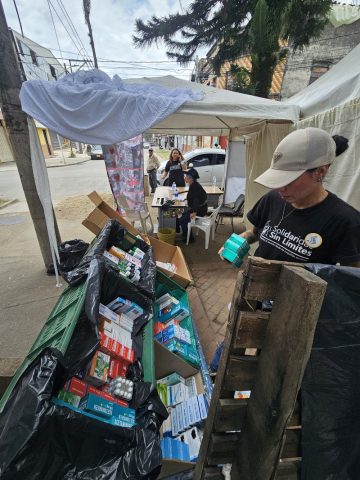 Volunteer sorts boxes of donated medicines in crates at a street-side aid tent