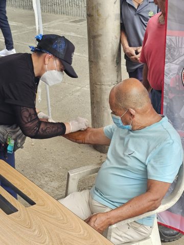 Masked volunteer in gloves cleans an older man’s forearm at an outdoor aid station