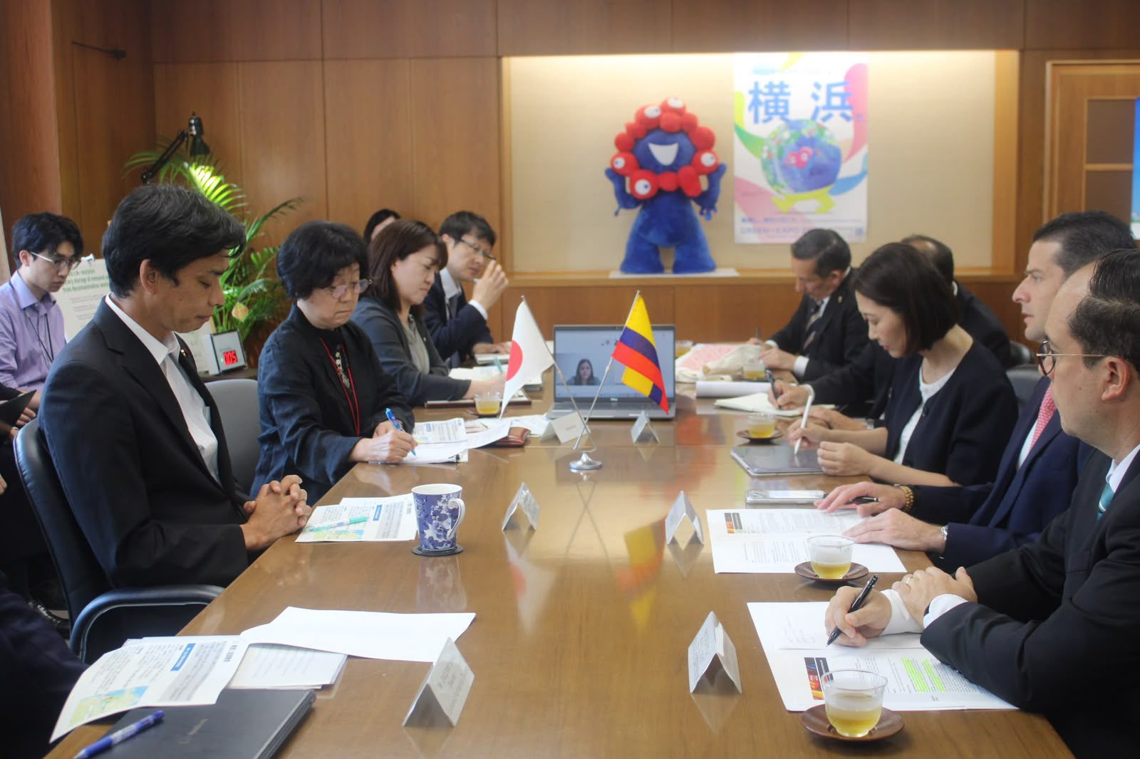 Japanese and Colombian delegations seated across a conference table with the two countries' flags and a laptop between them