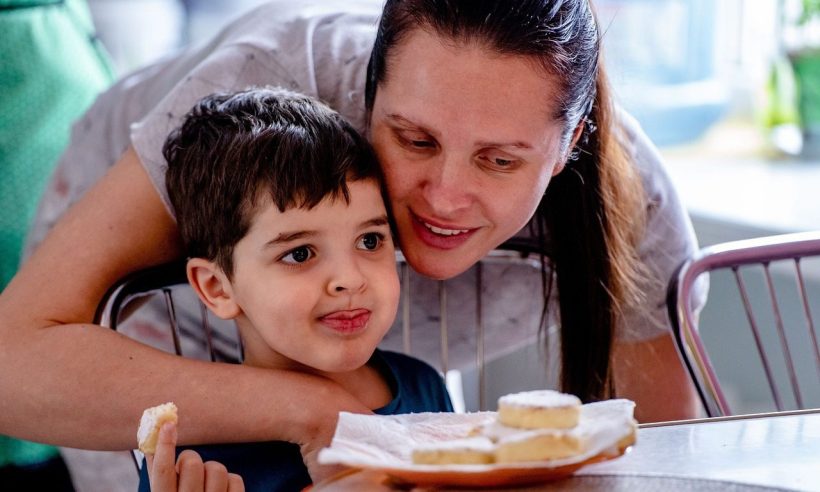 A mother embraces her young son at a cafe table set with pastries during breakfast.