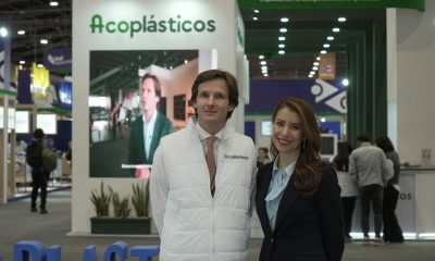 Daniel Mitchell in a white Acoplásticos vest and Ana Garibello in a dark blazer standing at a plastics trade fair booth