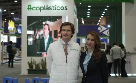 Daniel Mitchell in a white Acoplásticos vest and Ana Garibello in a dark blazer standing at a plastics trade fair booth