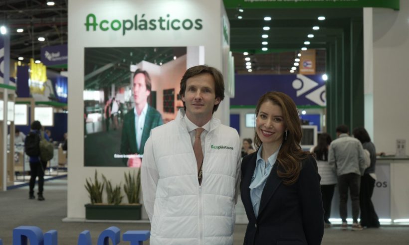 Daniel Mitchell in a white Acoplásticos vest and Ana Garibello in a dark blazer standing at a plastics trade fair booth