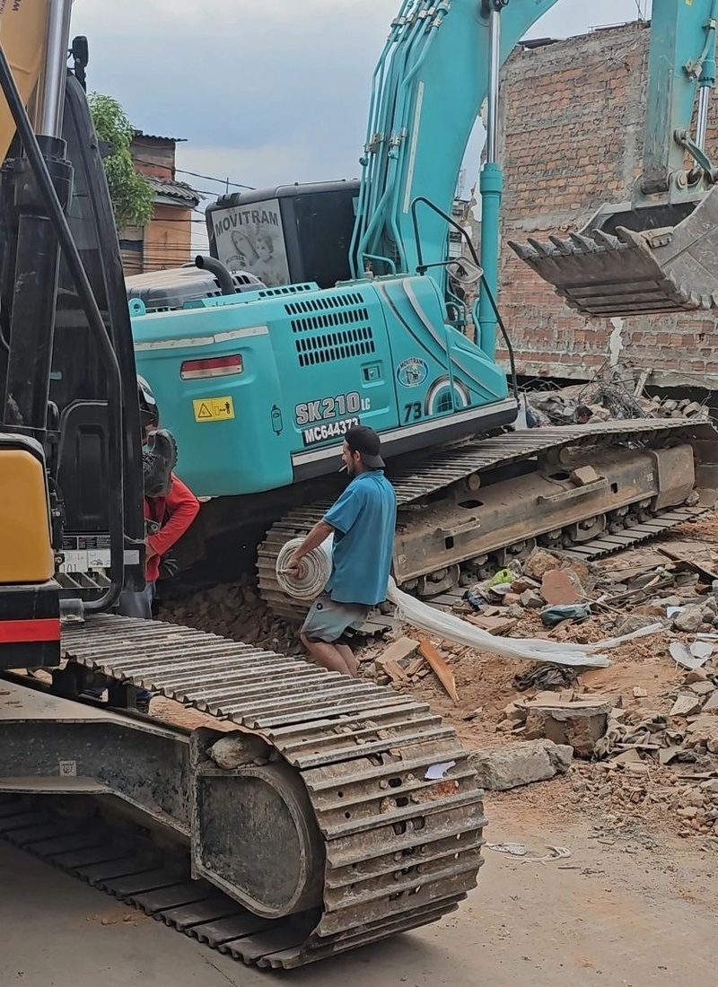 Excavator demolishes a collapsed building as a worker carries cable through the rubble in Pereira.