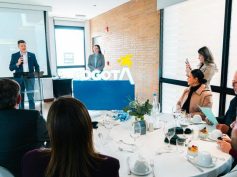A speaker at a podium addresses guests seated at round tables in front of an illuminated Bogotá sign.