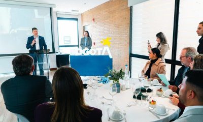 A speaker at a podium addresses guests seated at round tables in front of an illuminated Bogotá sign.