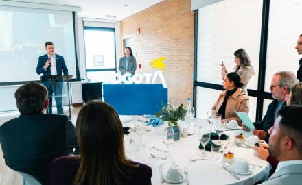 A speaker at a podium addresses guests seated at round tables in front of an illuminated Bogotá sign.