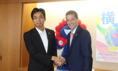 Colombian Minister Mauricio Gómez Amín and Japanese State Minister Toshiro Ino shake hands in front of a GREEN×EXPO 2027 mascot and poster
