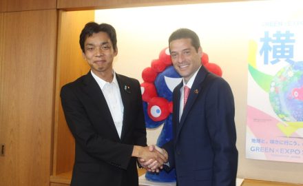 Colombian Minister Mauricio Gómez Amín and Japanese State Minister Toshiro Ino shake hands in front of a GREEN×EXPO 2027 mascot and poster
