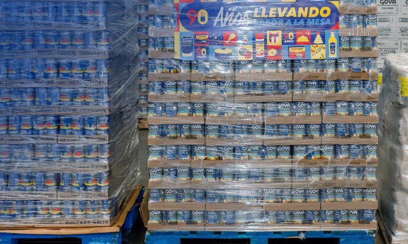 Shrink-wrapped pallets of canned Goya tomato sauce and mixed vegetables stacked in a warehouse.
