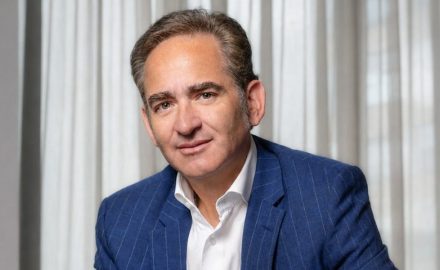 Portrait of Joaquín Gutiérrez Caballero in a blue pinstripe blazer and white shirt in front of light curtains