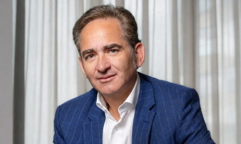 Portrait of Joaquín Gutiérrez Caballero in a blue pinstripe blazer and white shirt in front of light curtains