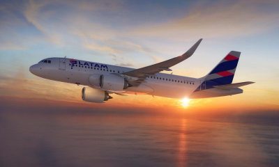 A LATAM Airlines Airbus A320neo banking in flight over the ocean at sunset, with clouds in the sky.