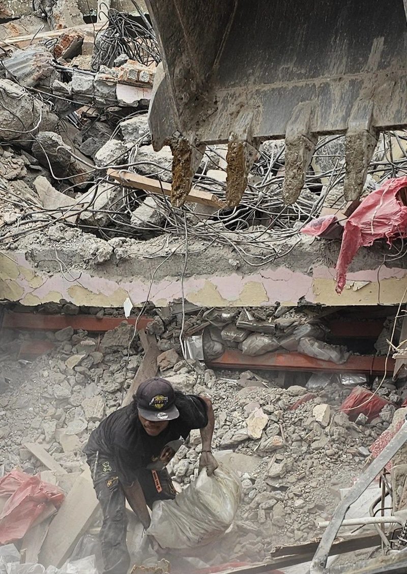 A man drags a sack of salvaged plastic bags out from under an excavator bucket.