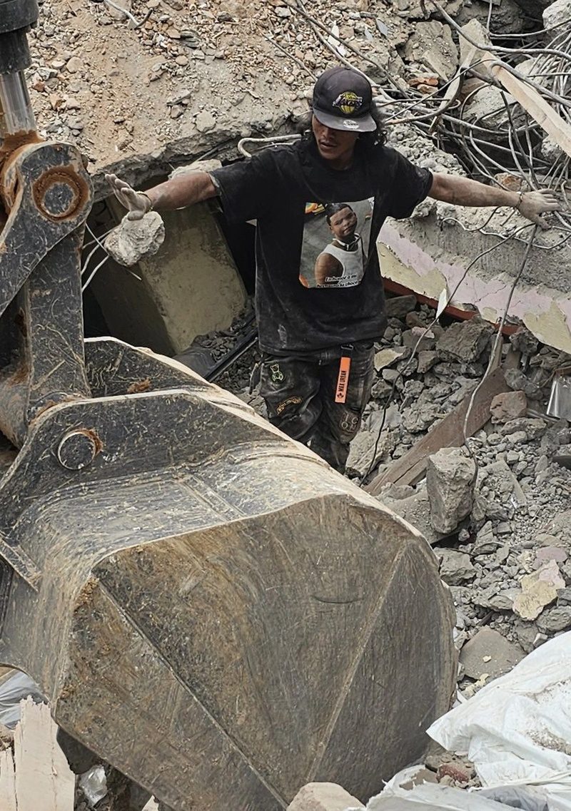 A man stands amid rubble beneath an excavator bucket at the collapsed factory site.
