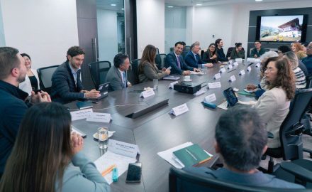 Tourism guild representatives and ministry officials seated around a long conference table with a screen showing a rural scene
