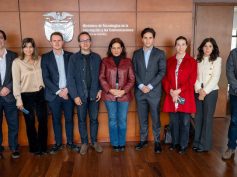 Nine people in business attire stand in a row before a wood-paneled wall with Colombia's coat of arms and the MinTIC name.
