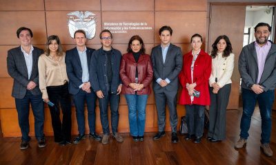 Nine people in business attire stand in a row before a wood-paneled wall with Colombia's coat of arms and the MinTIC name.