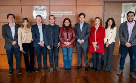 Nine people in business attire stand in a row before a wood-paneled wall with Colombia's coat of arms and the MinTIC name.
